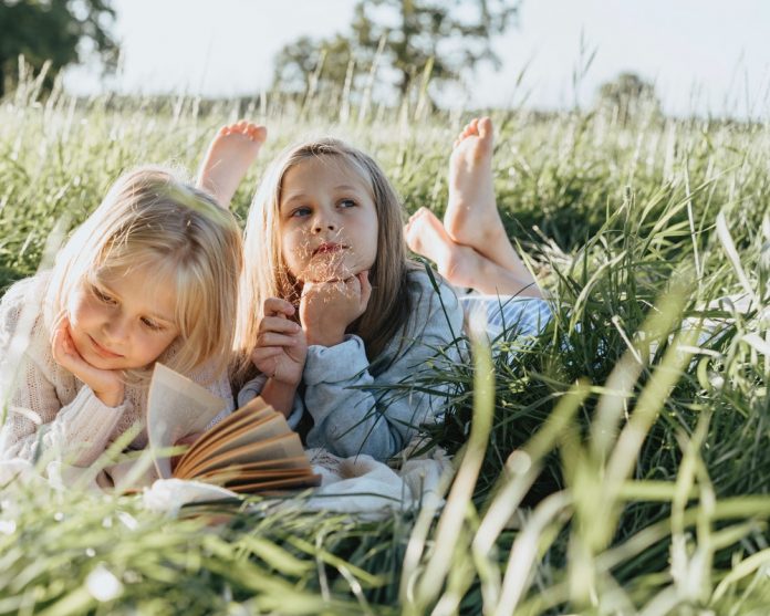 dve-devojčice-čitaju-na-travi